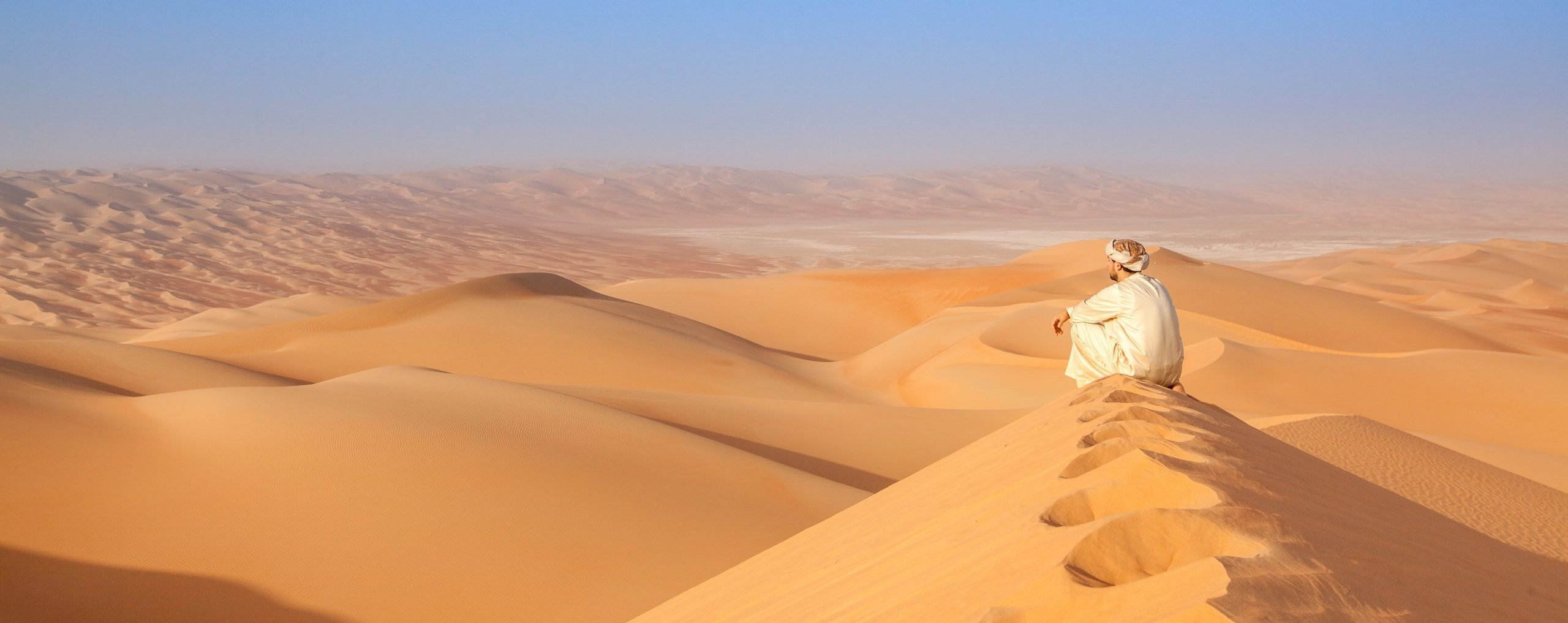 A man sitting on a sand dune looking into the distance